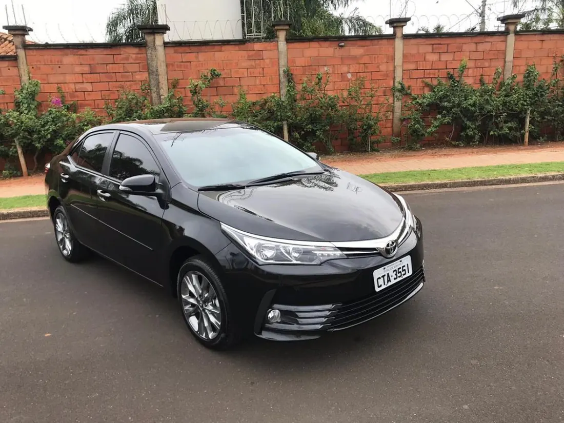 Toyota Corolla preto da frota executiva, visto de frente, estacionado em rua arborizada