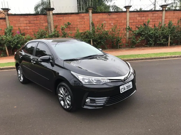 Toyota Corolla preto da frota executiva, visto de frente, estacionado em rua arborizada