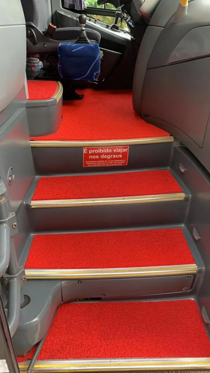 Degraus internos de um ônibus da frota, com carpete vermelho e aviso de segurança proibindo viajar nos degraus