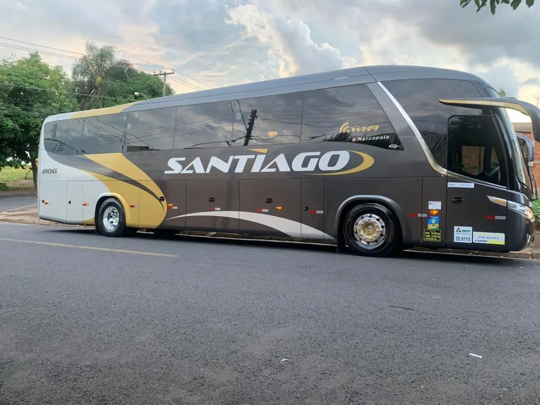 Ônibus rodoviário da Santiago, com grafismo dourado e cinza, estacionado e visto de lado