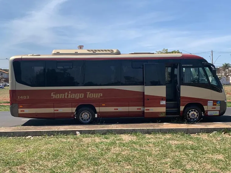 Micro-ônibus Santiago Tour, pintura vermelha e creme, estacionado sobre a grama