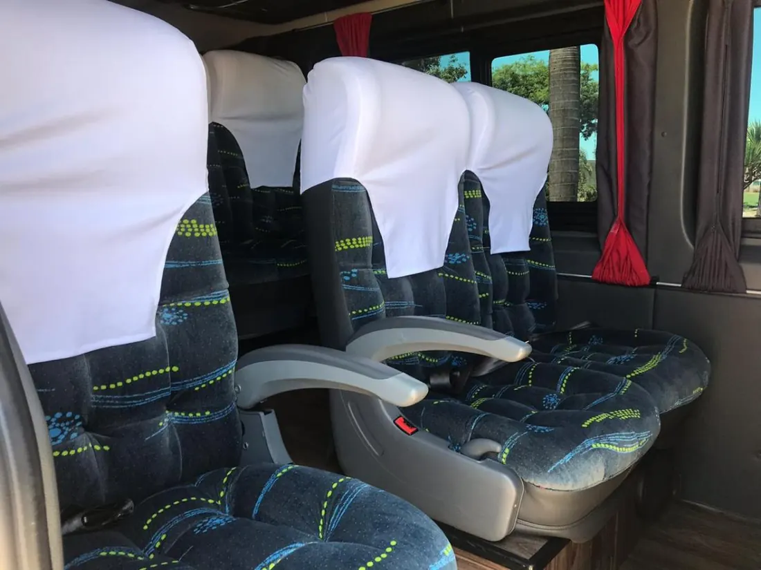 Poltronas de ônibus da frota, com capas brancas de encosto e cortina vermelha na janela