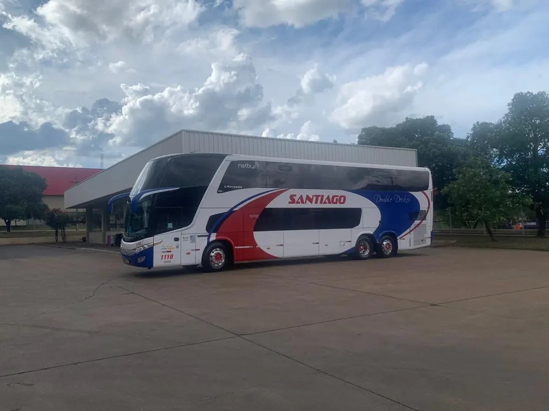 Ônibus de dois andares da Santiago, pintura branca com faixas vermelha e azul, estacionado no pátio