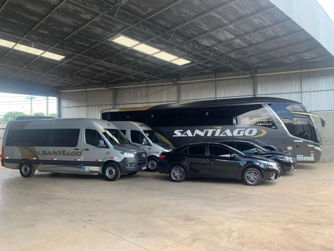 Frota reunida sob o galpão da empresa: ônibus executivo, vans e carros pretos lado a lado